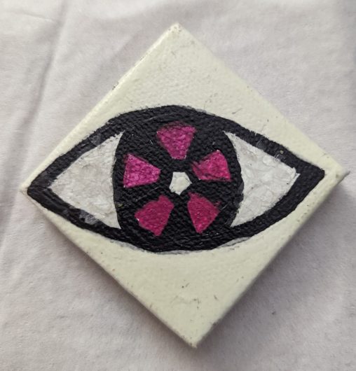 A very simple icon of an eye painted onto a 2-in by 2-in diamond canvas. The white of the eye is covered in glitter, the iris of the eye is made of purple and black slices.